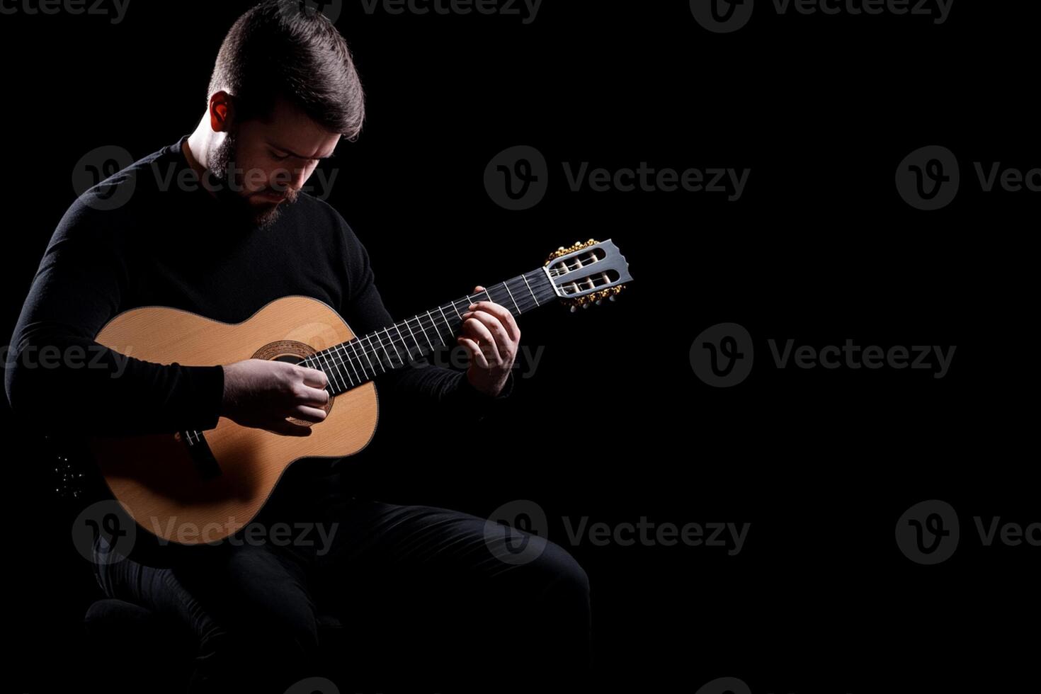 A man is playing an acoustic guitar on a black background photo