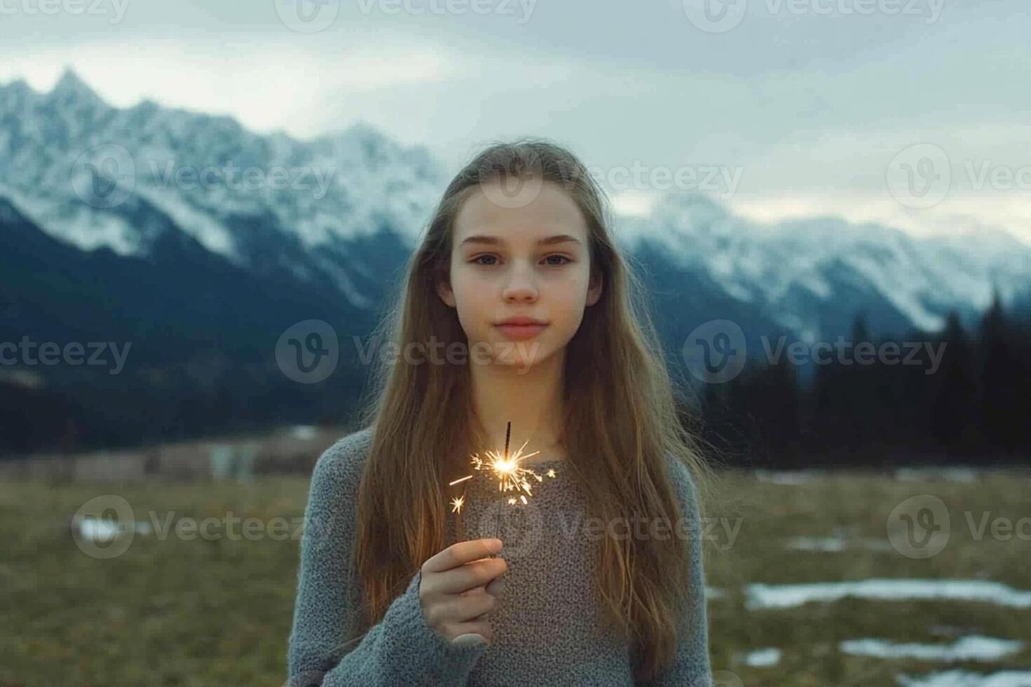 A girl holding a sparkler in front of mountains photo