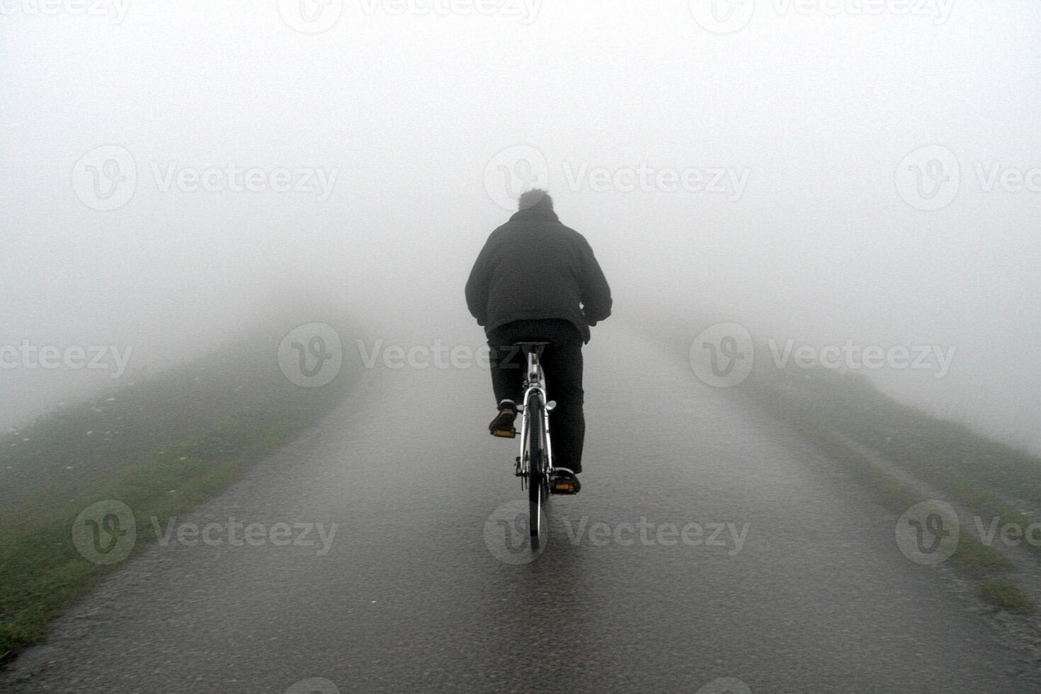 A person riding a bike down a foggy road photo