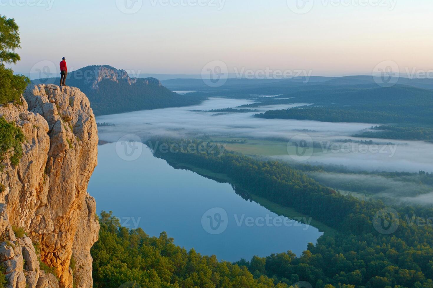 A man standing on a cliff overlooking a lake photo