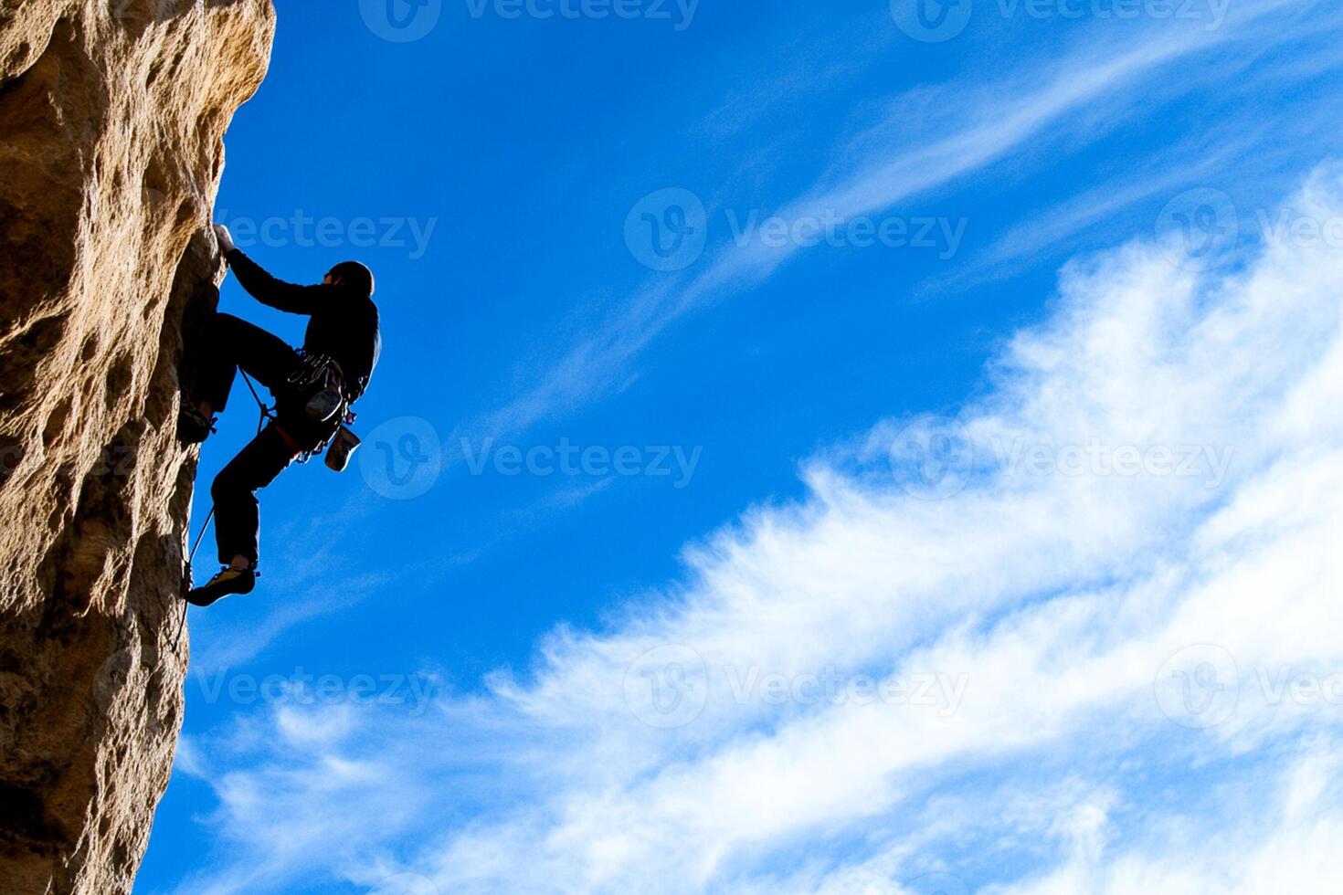 A man climbing on a rock in the middle of a blue sky photo