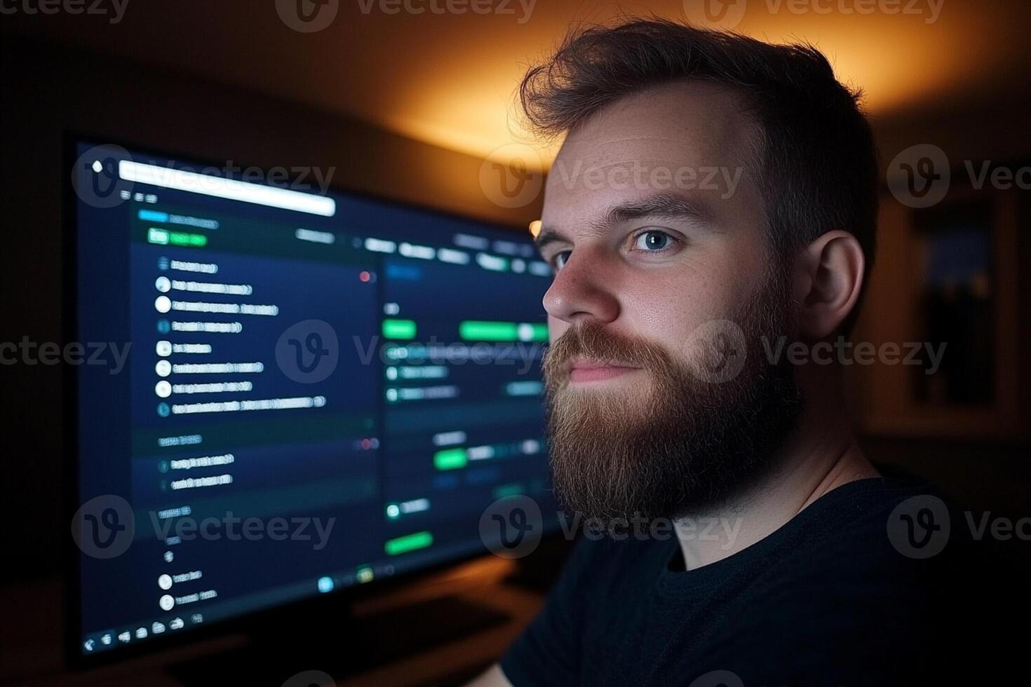 A man with a beard and a black shirt is looking at a computer screen photo