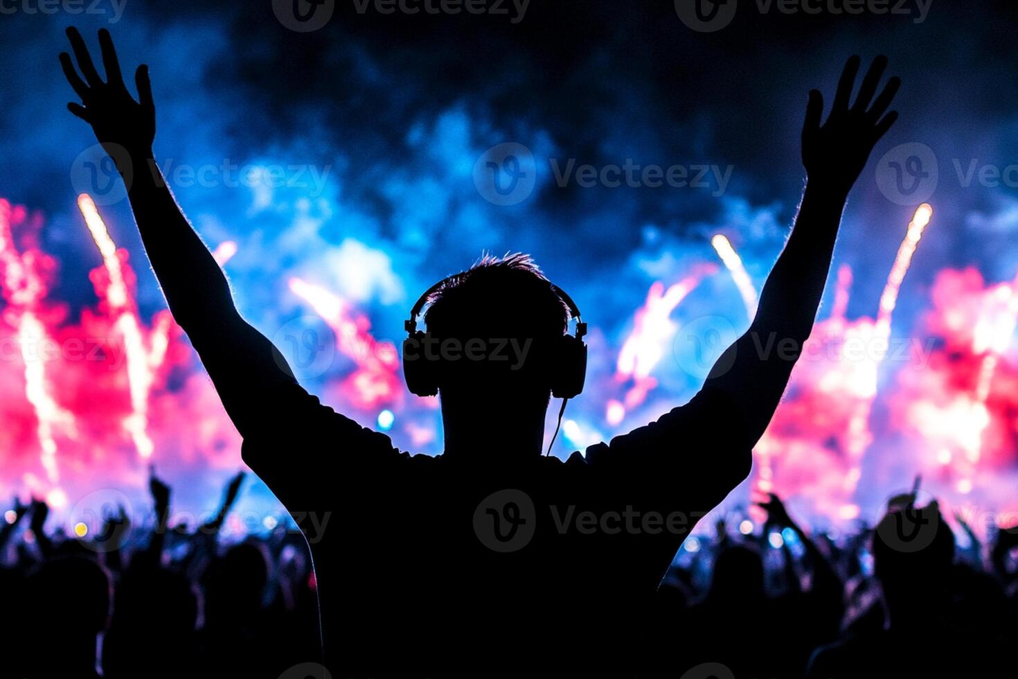 A person with headphones and arms up in front of a crowd photo