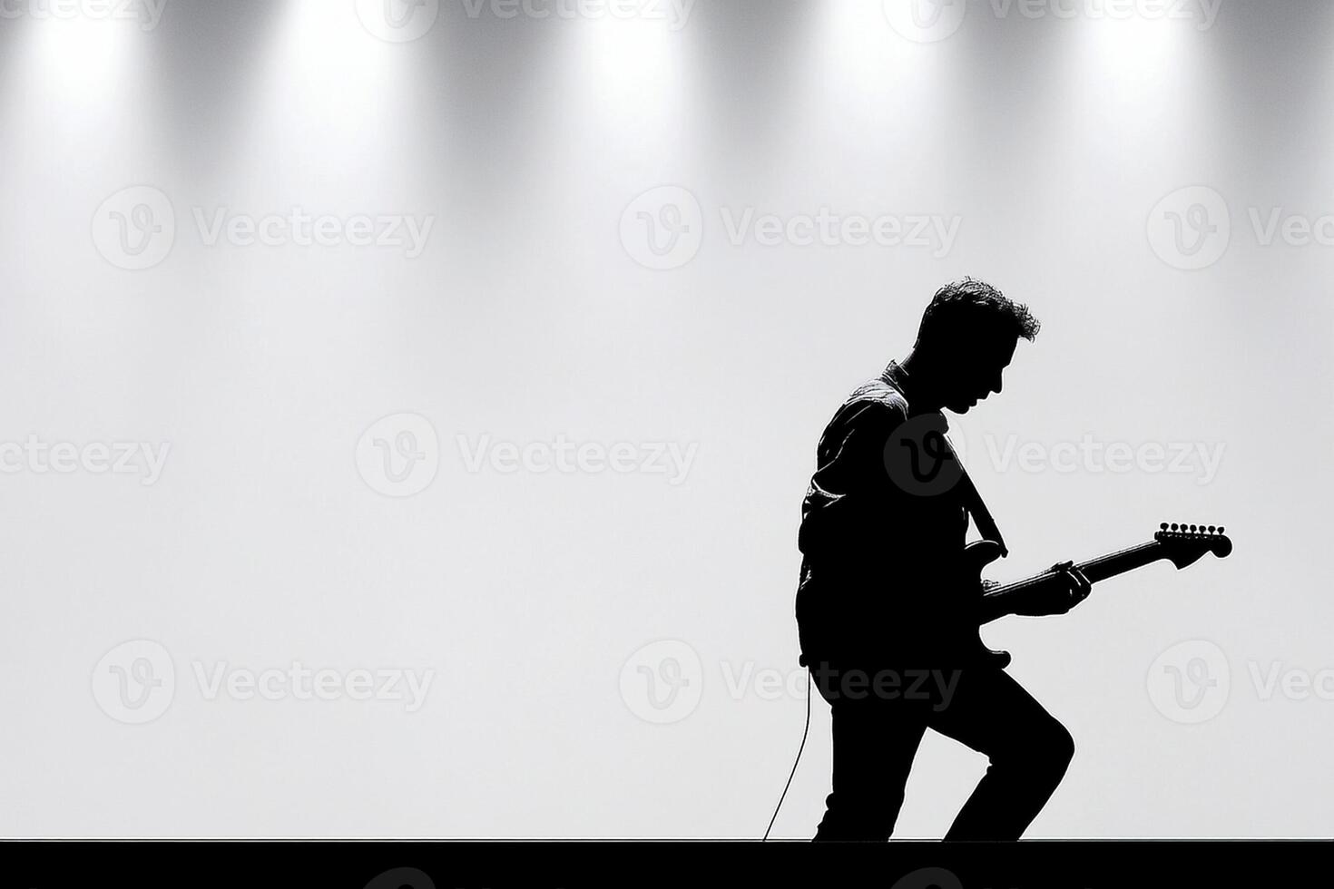 Silhouette of a man playing guitar in front of a spotlight photo