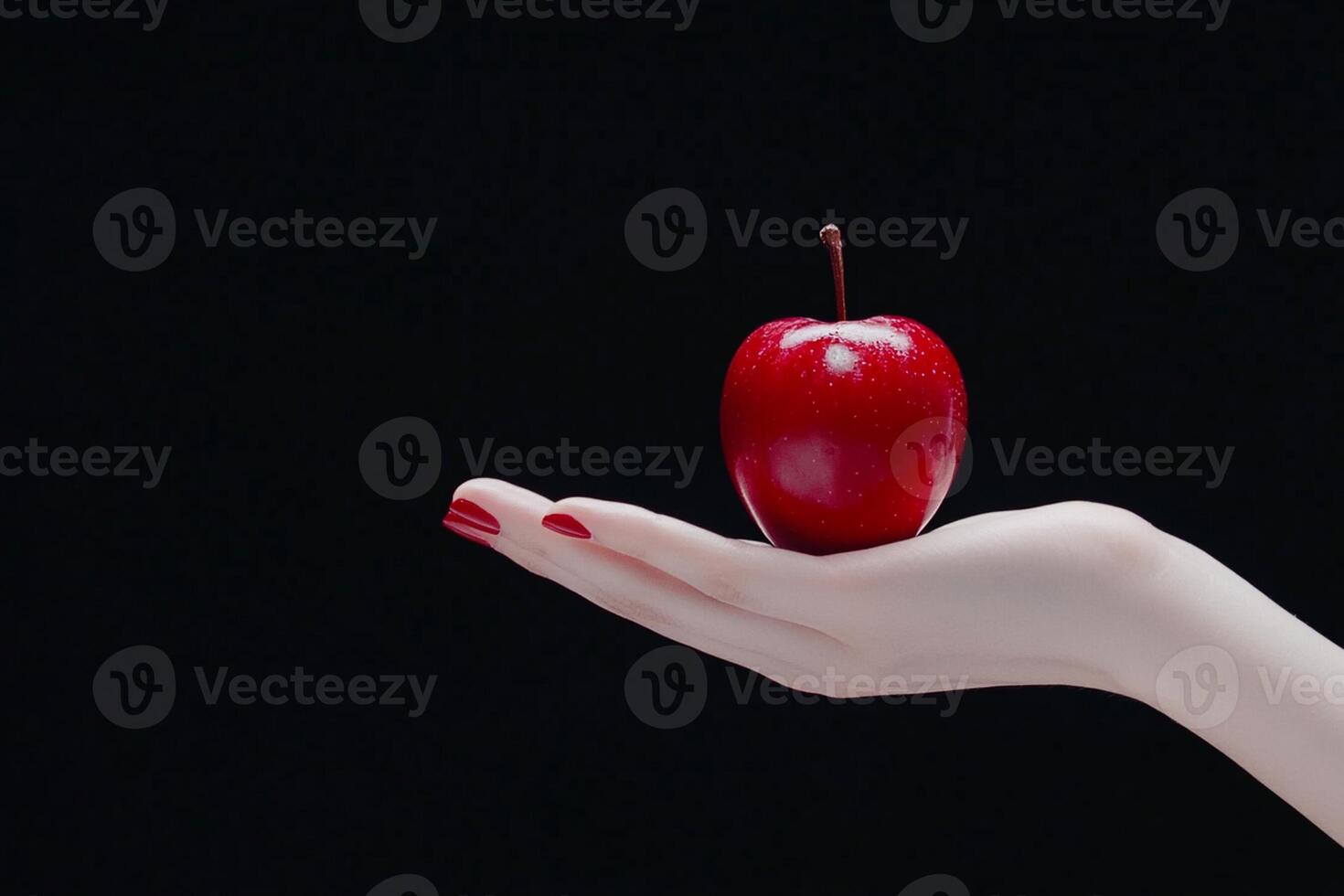 A woman's hand holding a red apple on a black background photo