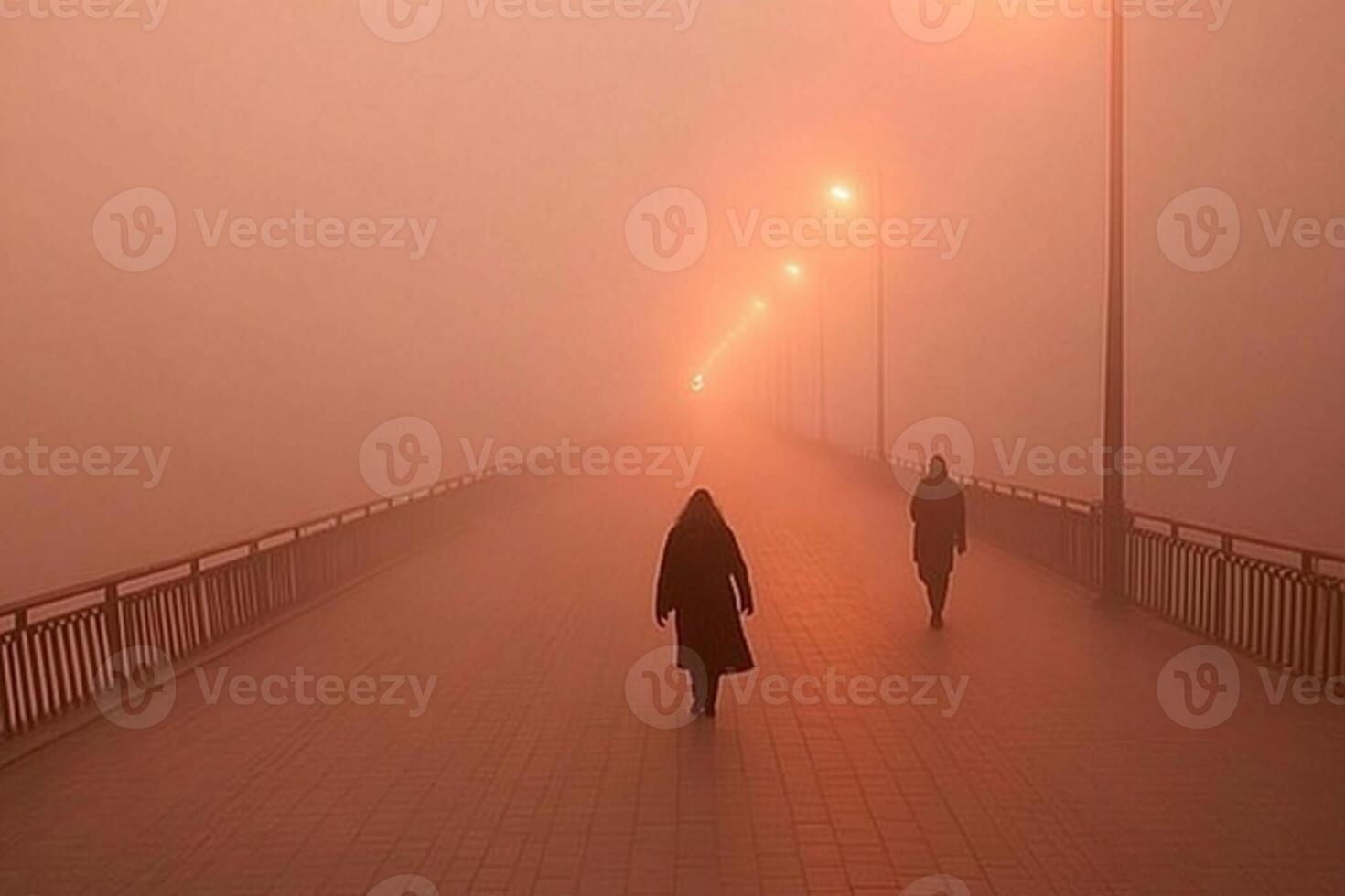 Two people walk across a foggy bridge at night photo