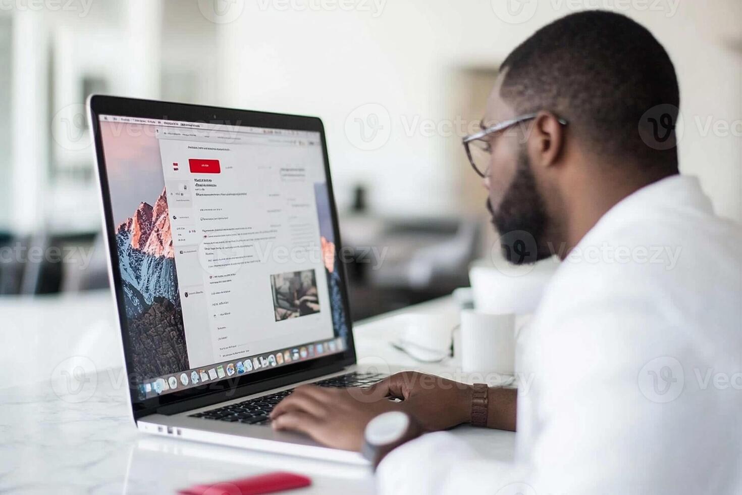 A man in a white shirt is sitting at a desk with a laptop photo