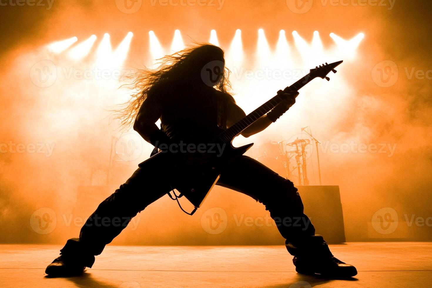 A man with long hair playing guitar in front of a spotlight photo