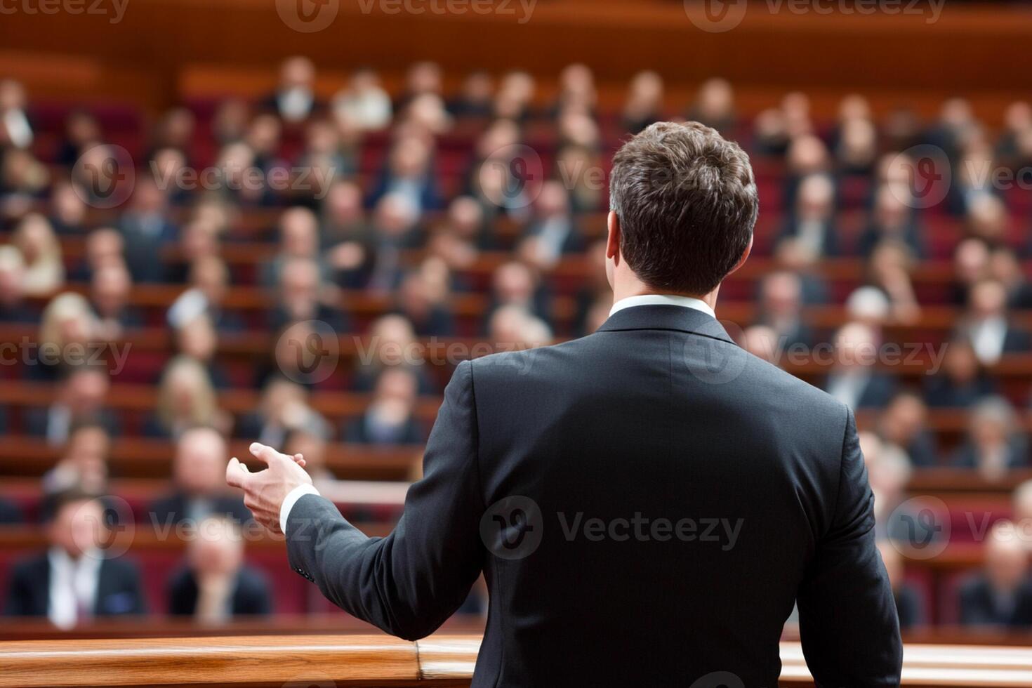 A man in a suit is giving a speech in front of a large audience photo