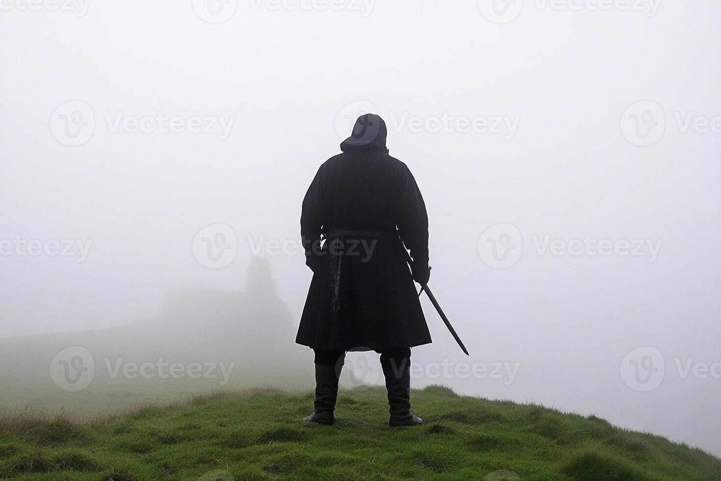 A man in a black cloak stands on a hill with a sword photo