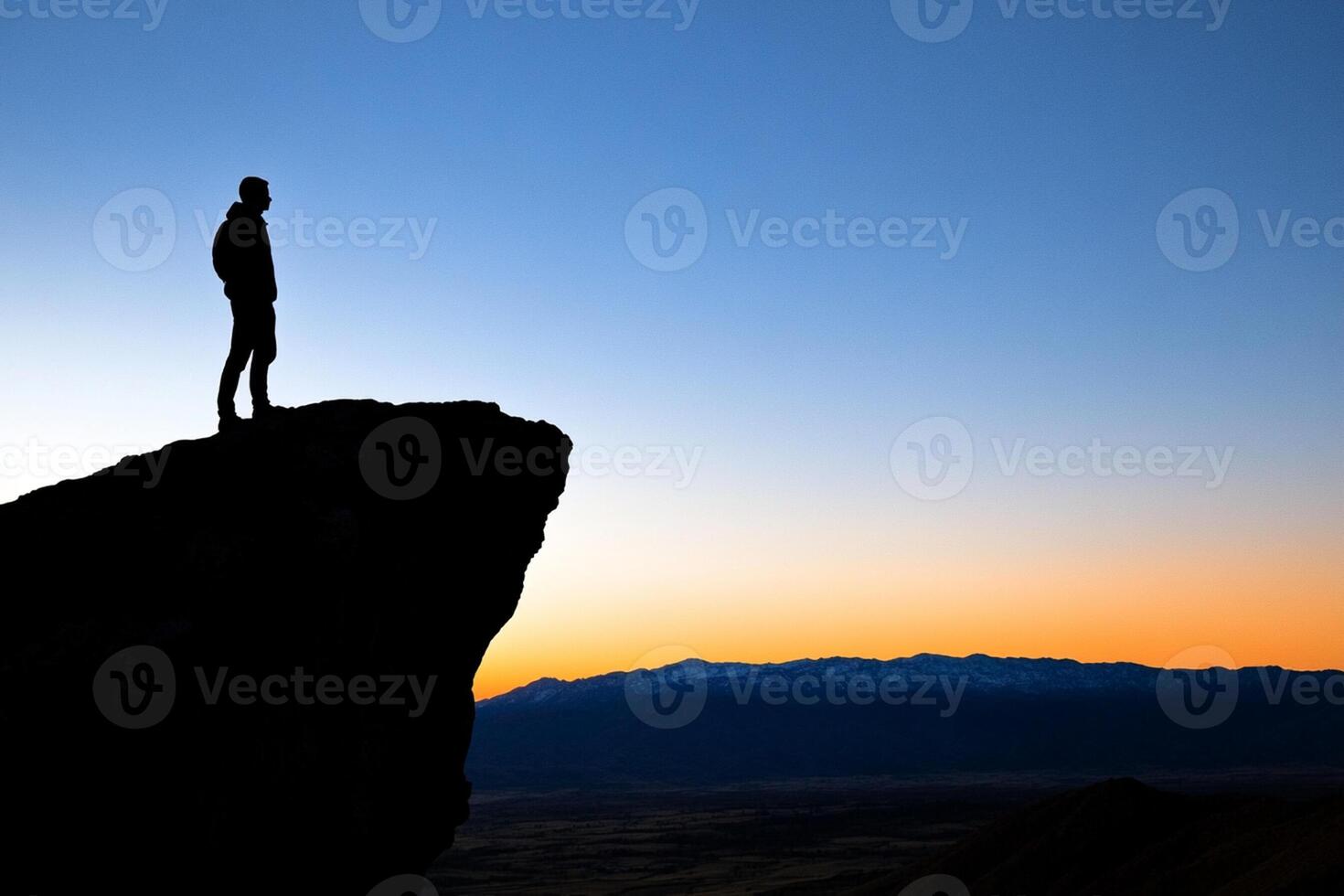 Silhouette of a man standing on top of a mountain at sunset photo