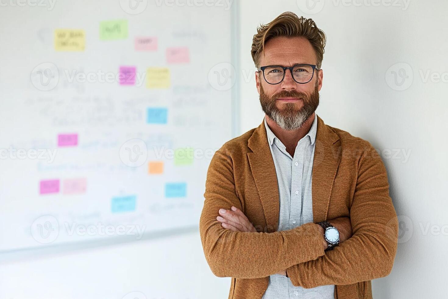 A man with glasses and a sweater standing in front of a whiteboard photo