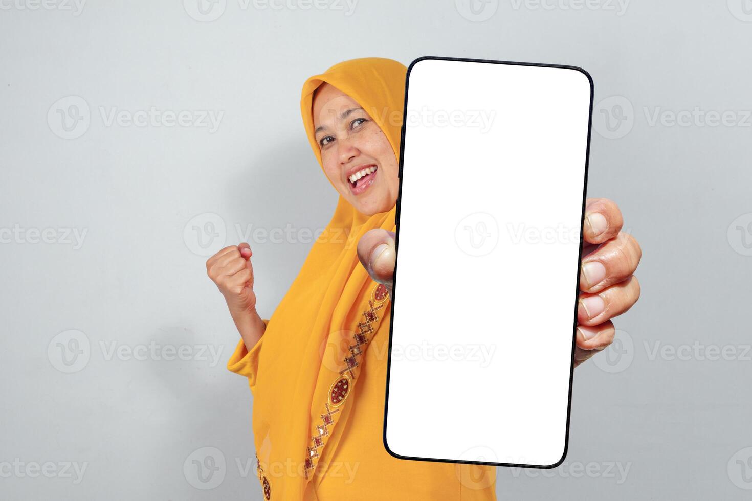 Excited Muslim woman in yellow hijab showing blank smartphone screen and celebrating photo