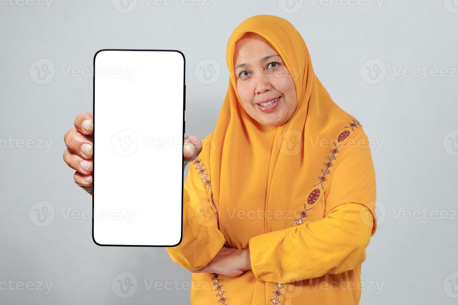 Smiling Muslim woman in yellow hijab showing smartphone with blank screen confidently photo