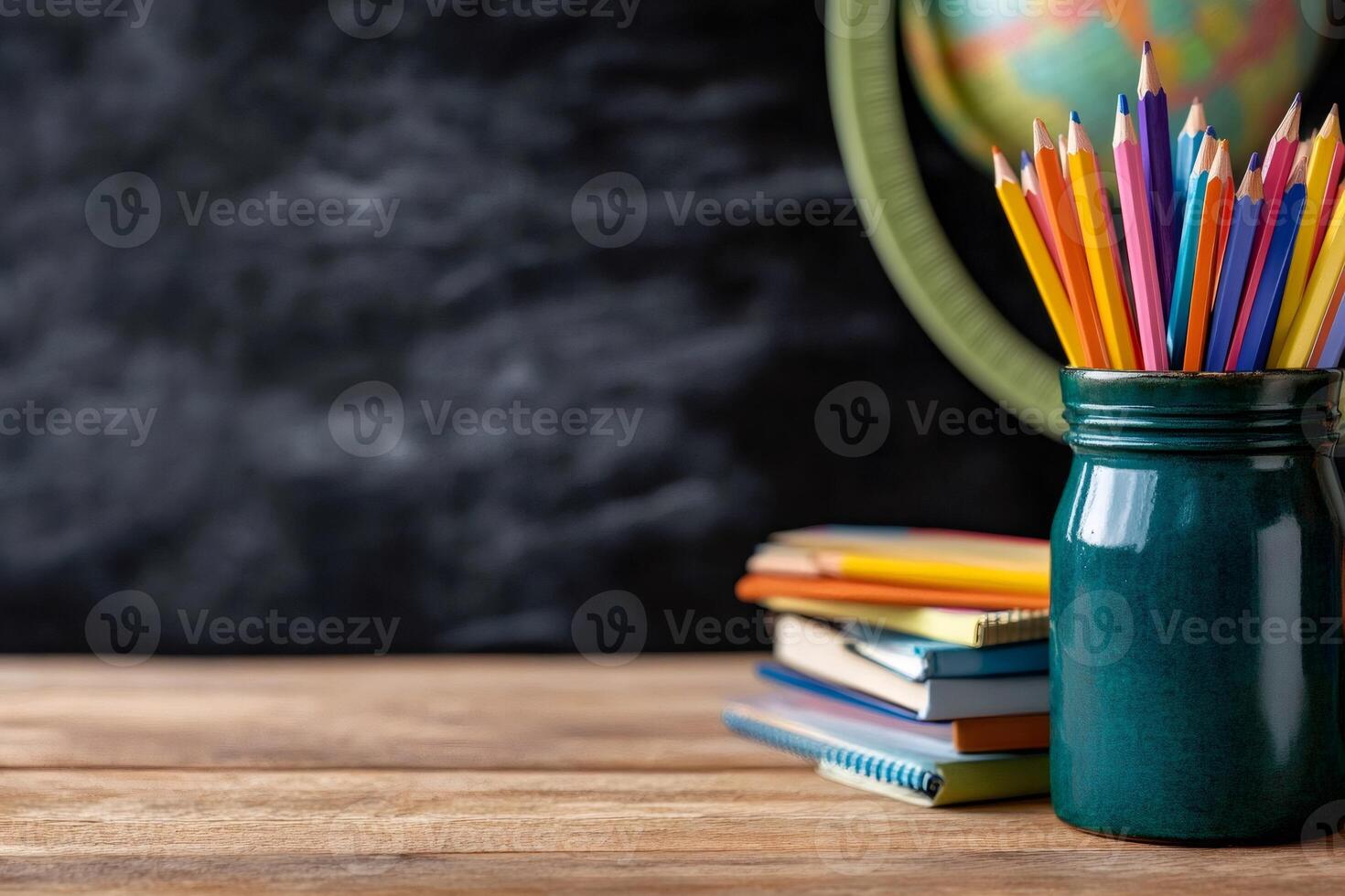 Back to school concept with colored pencils, notebooks and globe on teacher's desk in front of blackboard photo