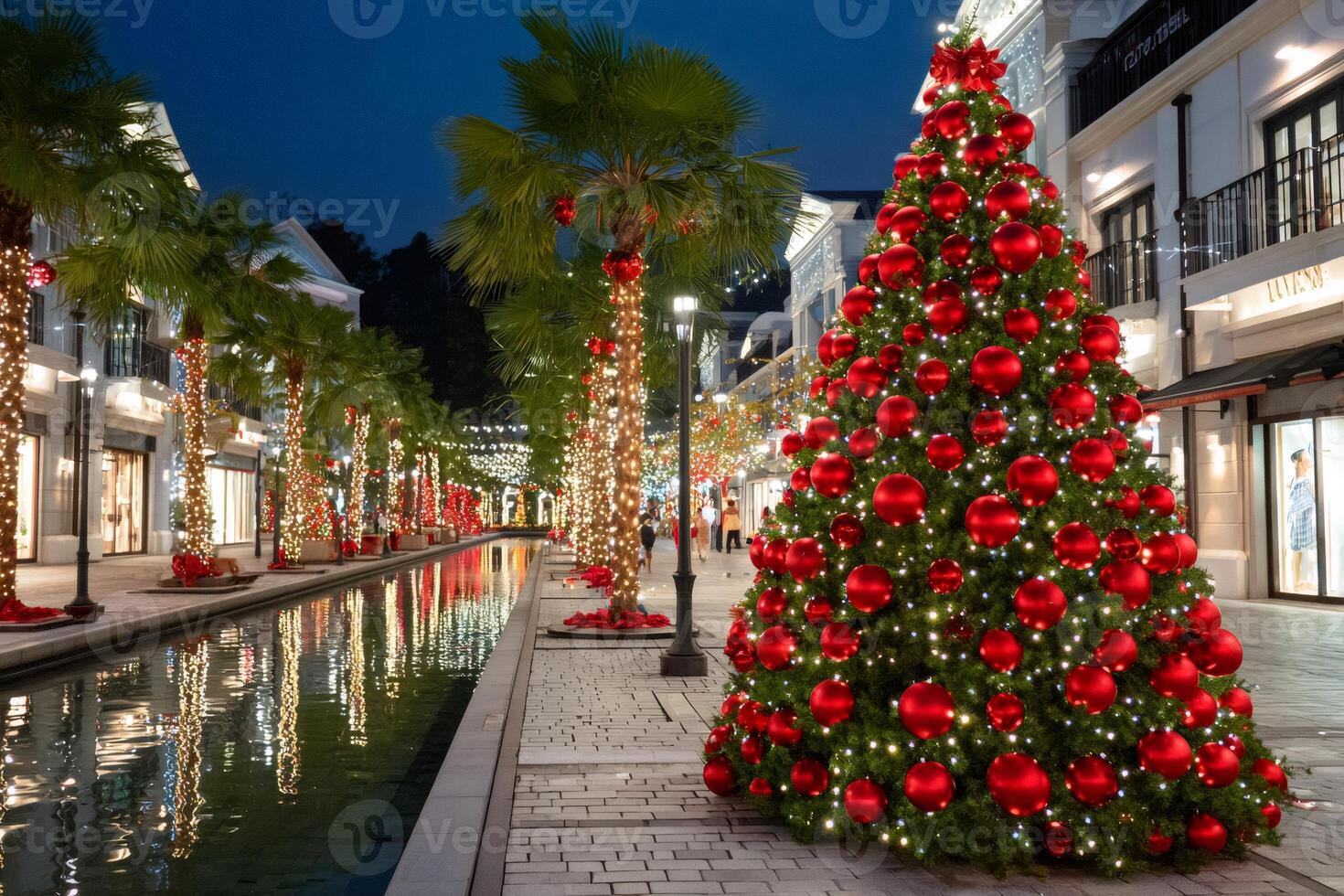 Christmas tree with red ornaments decorating a shopping mall with palm trees and a canal at night photo