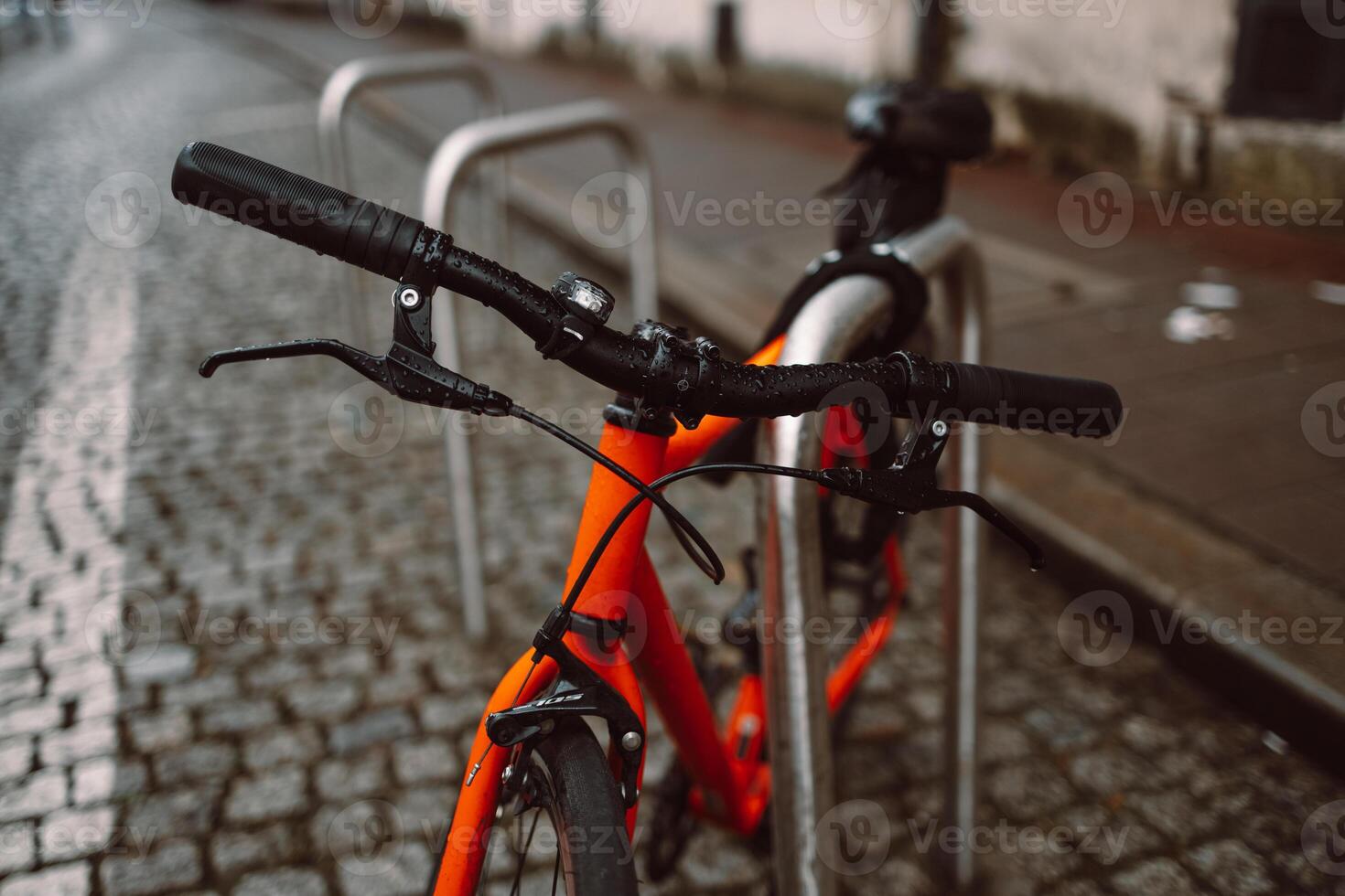 Handlebar View of an Orange Bicycle on Wet Cobblestones photo