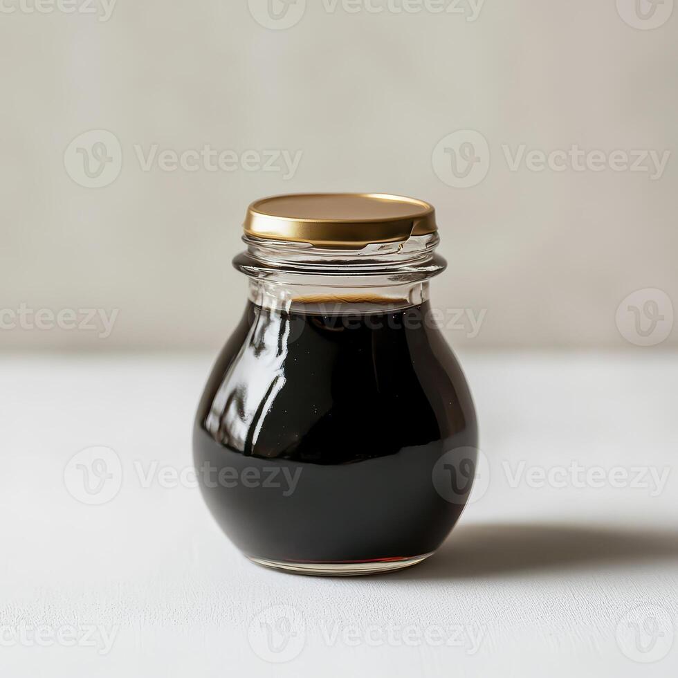 Dark syrup in a glass jar on a white surface photo