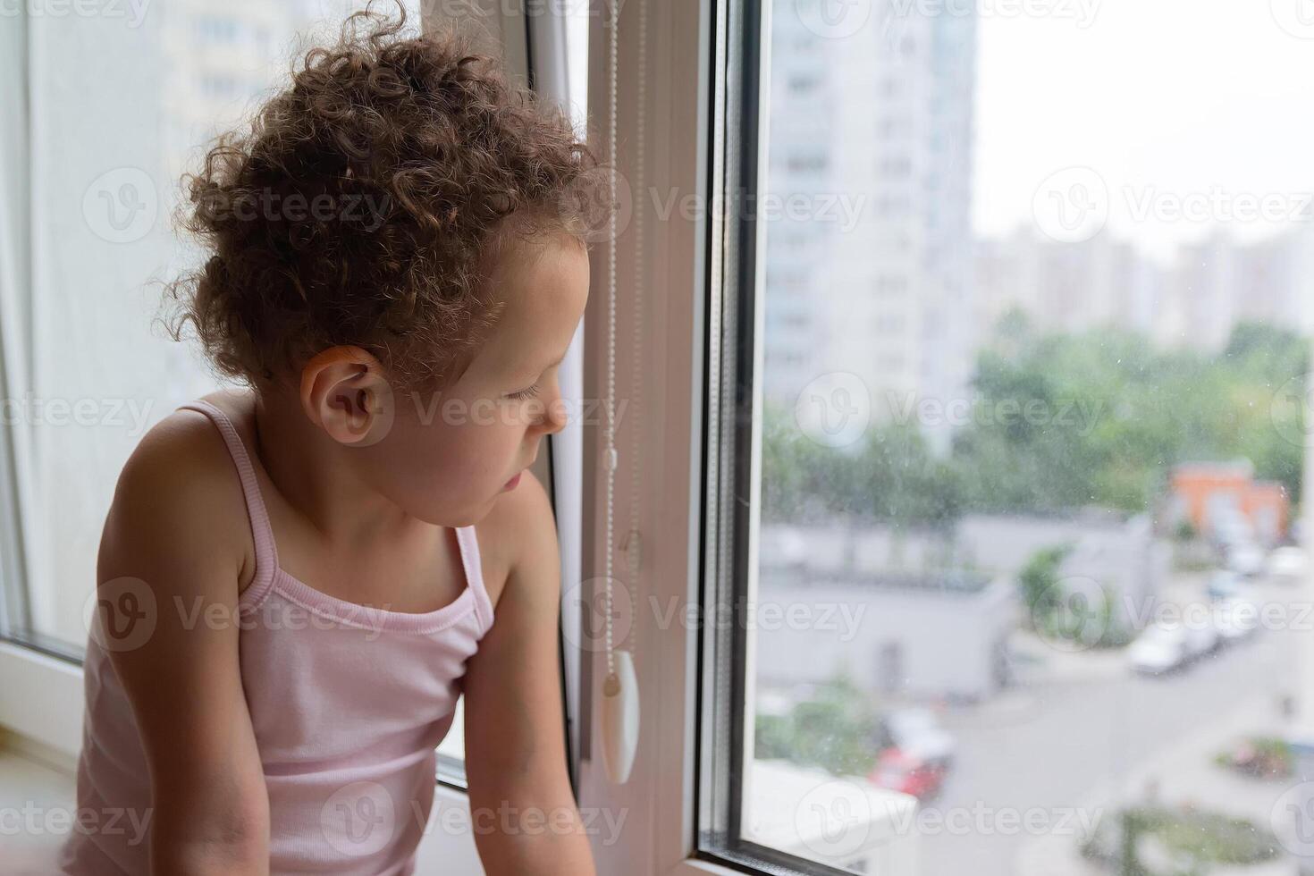 Curly child looks out the window sitting on the windowsill photo
