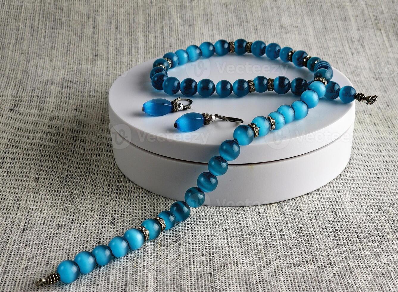 Set of necklace and earrings with blue cat's eye effect. White background. Zircon inserts photo