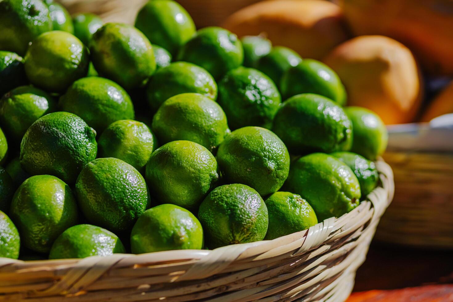 A close-up of fresh green limes in a woven basket, displayed under natural light at a market stand. Perfect for use in food-related content, gastronomy, nutrition, and local agriculture promotions. photo