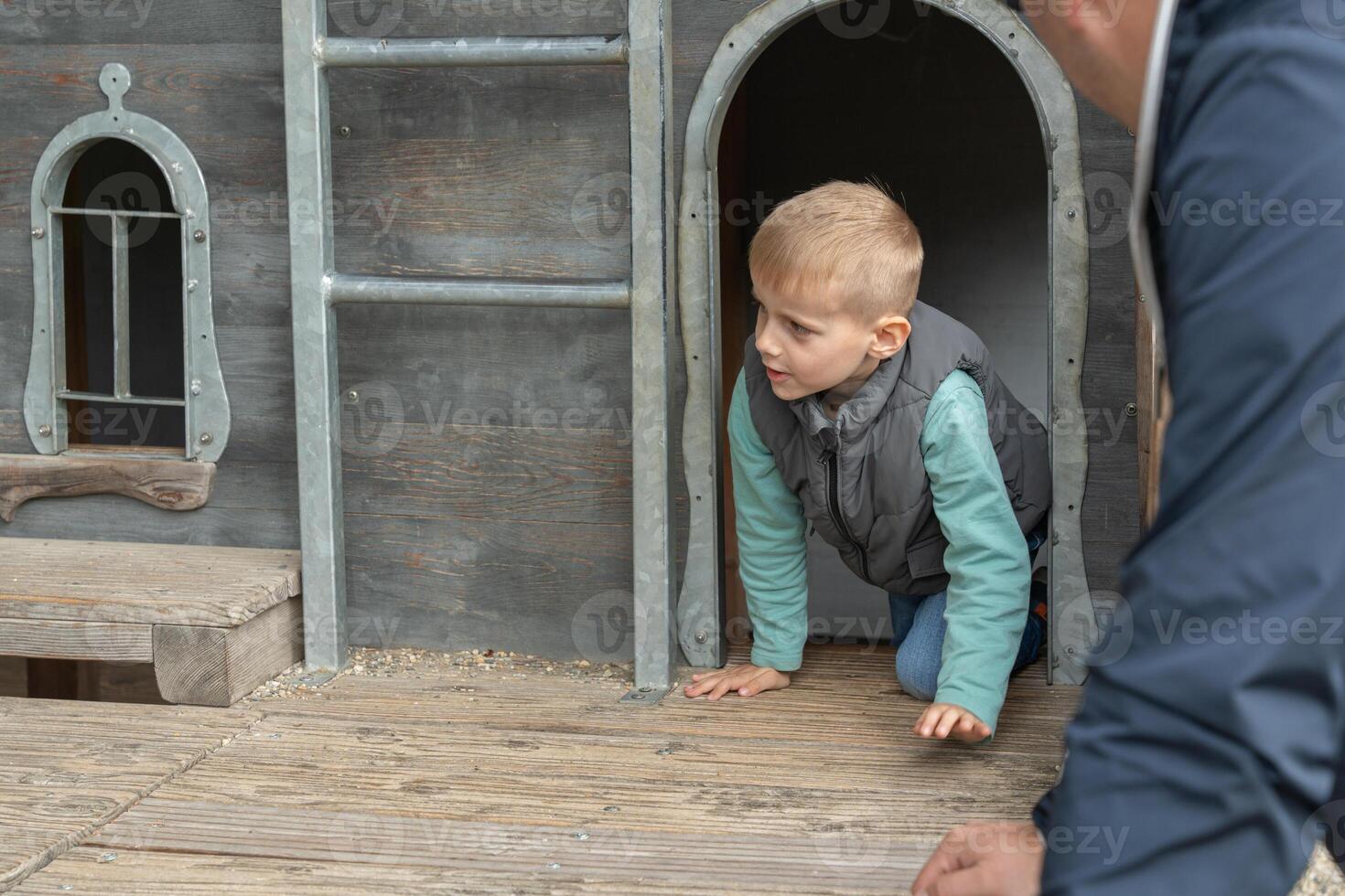 Child Crawling Out of Wooden Playhouse Door with Adult Nearby photo