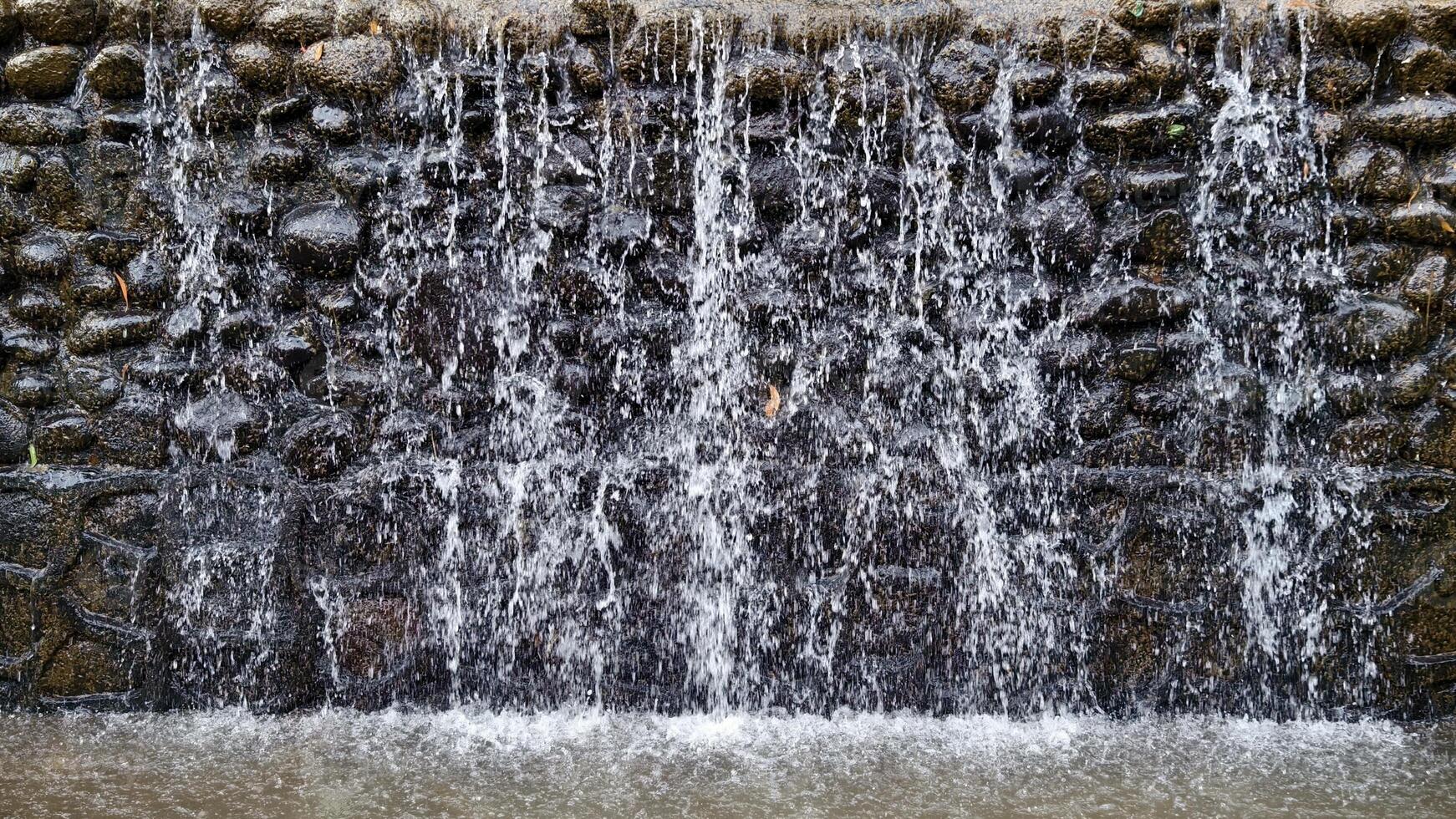 Artificial Waterfall with Cascading Water Over a Textured Rock Wall Feature in a Park photo
