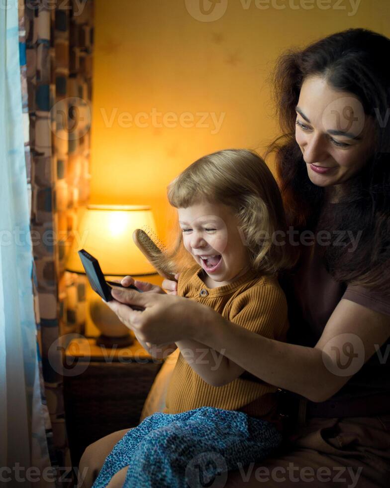 Happy mother and daughter comb their hair and look in a mirror. Morning routine. photo