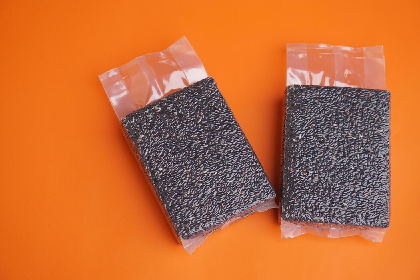 Two packages of 1kg black riceberry in sealed vacuum bag, on orange background. Concept, eco-friendly organic grain, rich in nutrients, for export, health markets, and conscious consumers worldwide. photo