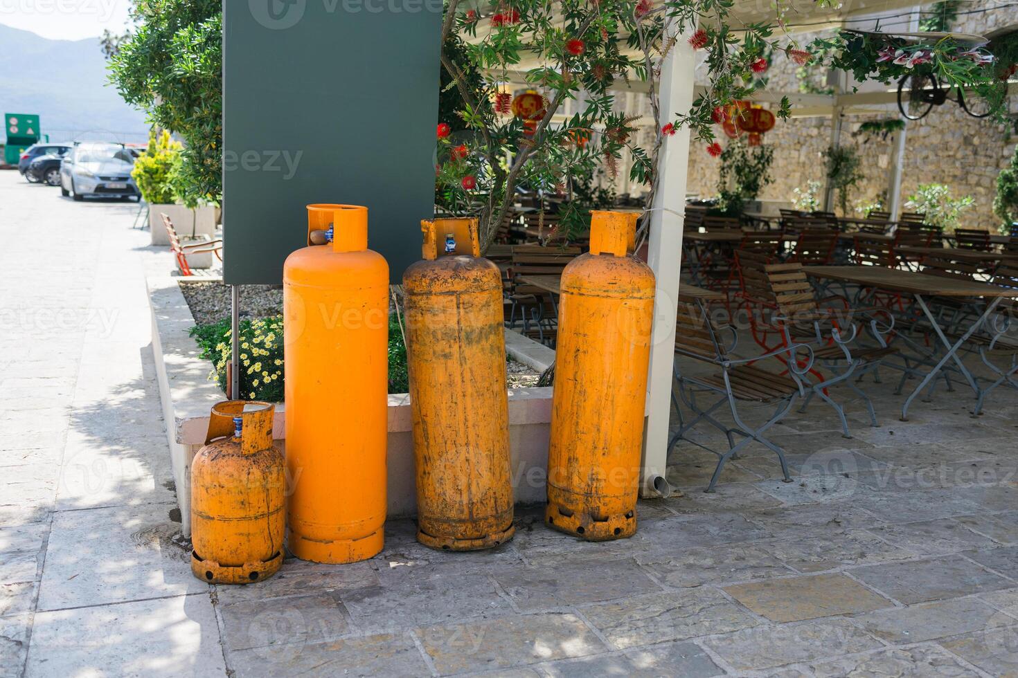 Outdoor storage of orange gas cylinders near cafe seating. Industrial utility, safety awareness, and restaurant operations. photo