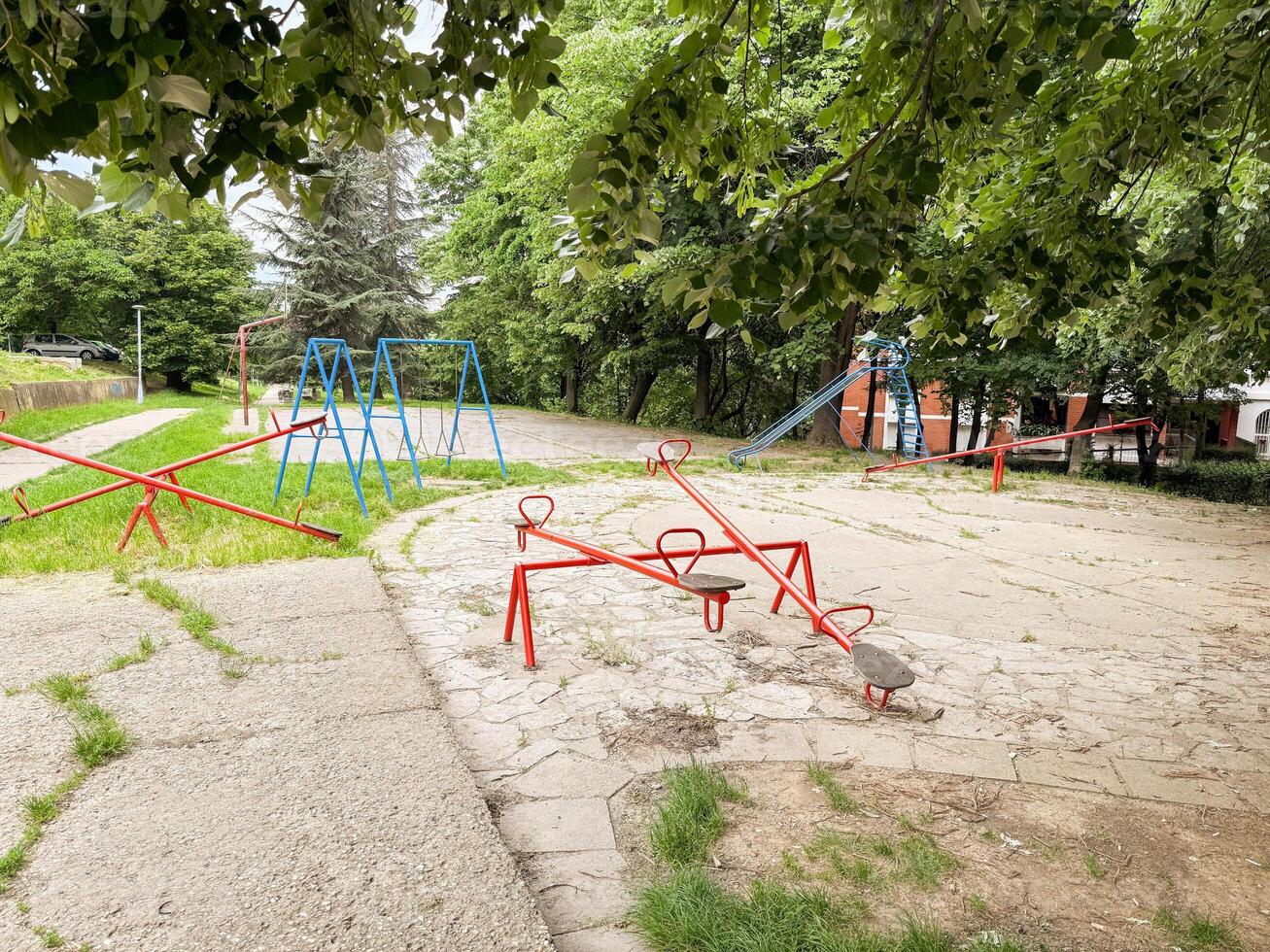 Empty retro playground with seesaws, swings, and a slide under green trees. A quiet and nostalgic public space in the city. photo