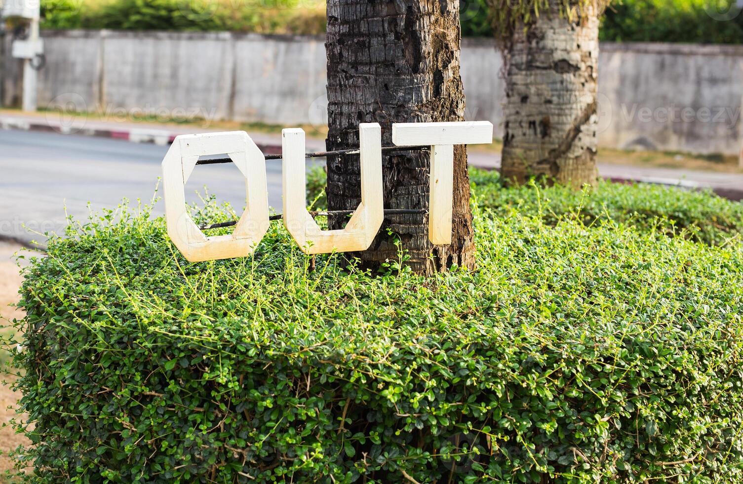 exit or out sign mounted on a green bush photo