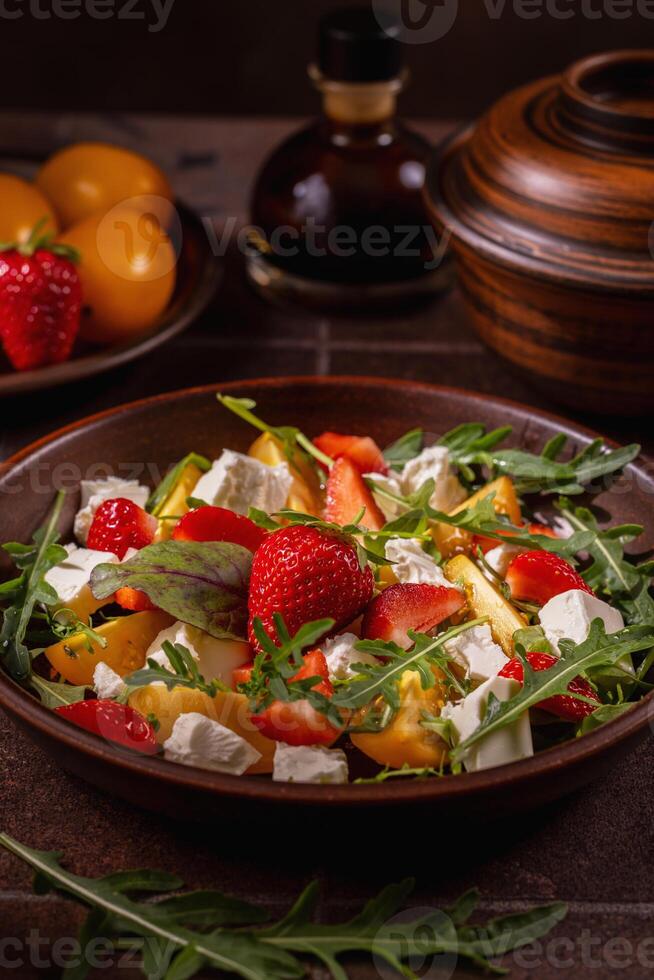 Delicious summer salad with strawberries, yellow tomatoes, feta cheese, arugula and balsamic vinegar dressing photo