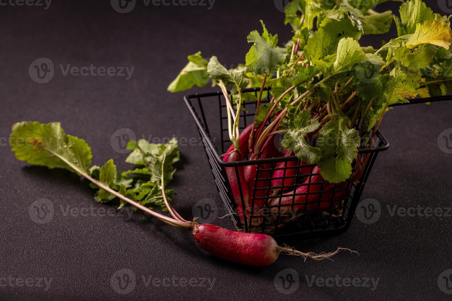 Freshly picked red radishes with green leaves spilling from a black metal basket photo