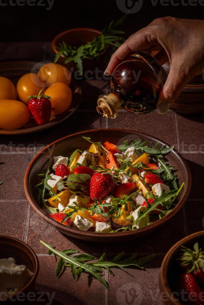 Chef pouring balsamic vinegar onto fresh summer salad with strawberries and cheese photo