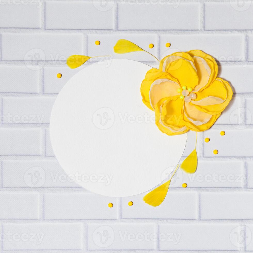 White Square Background With Handmade Gentle Yellow Flower and Feathers, Lying Flat on the White Brick Wall, Top View. Have an Empty Circle Place For Your Text. photo