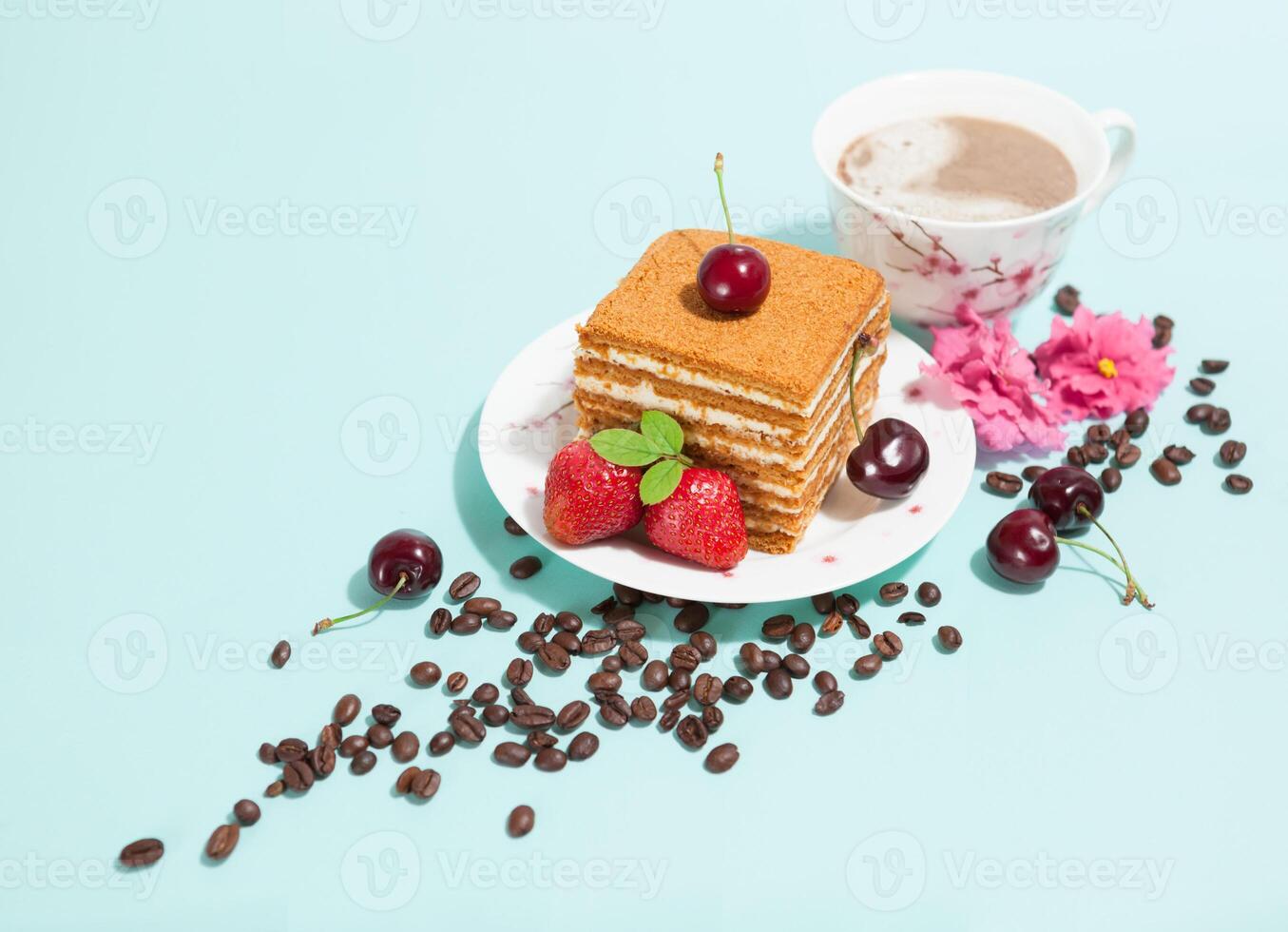 Tasty piece of cake on the white plate and cup of coffee,decorated with flowers,coffee beans,strawberries and cherry on the light mint background with empty place,perspective view,diagonal composition photo