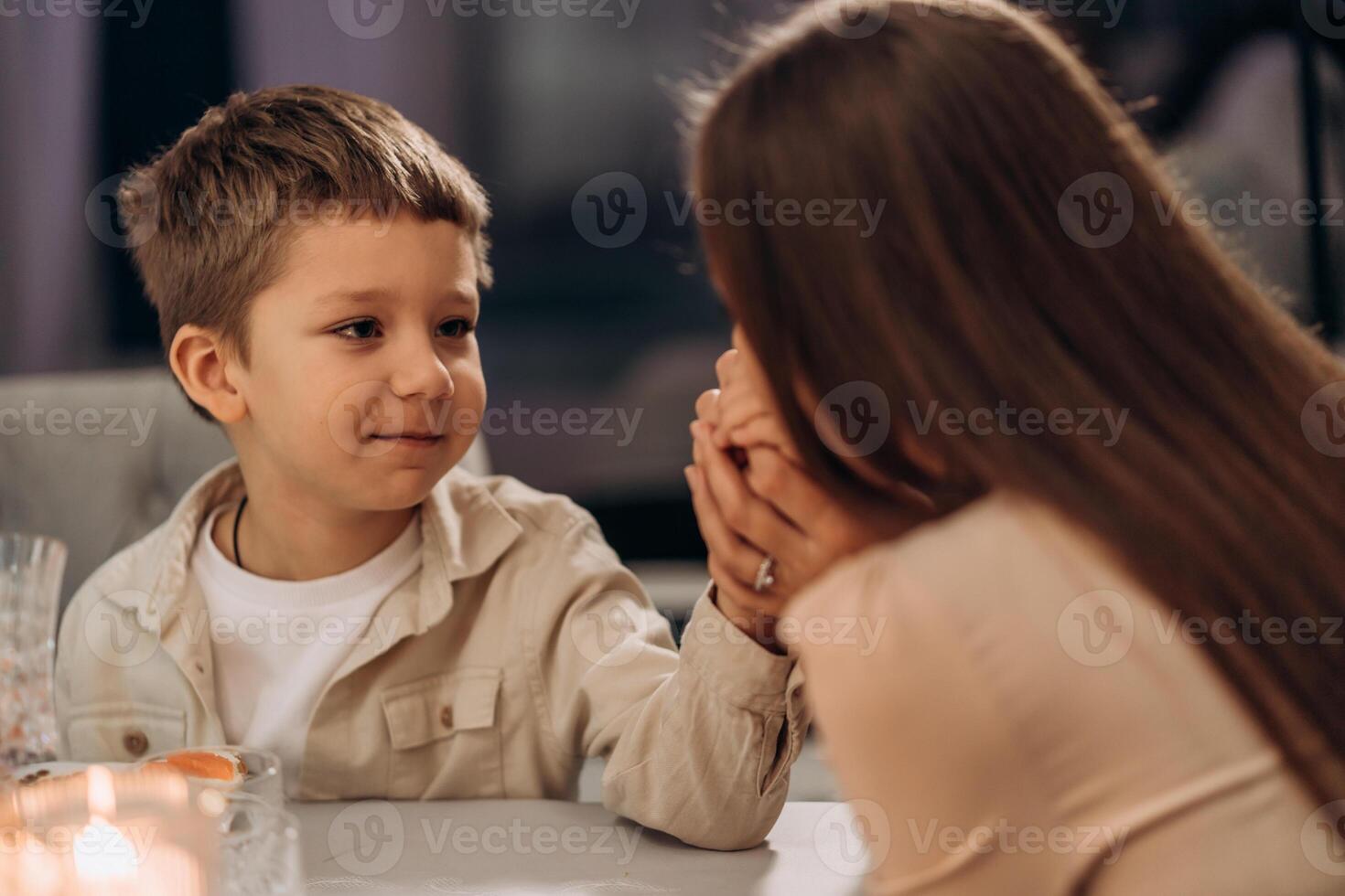Calm and loving boy holds his mothers hands while looking into her eyes across candlelit dinner table capturing a quiet moment of trust support and affection ideal for Valentines family concept or photo