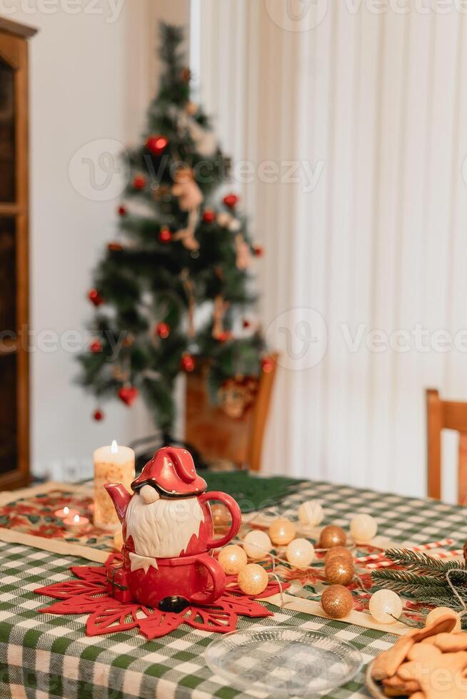 Warm cozy Christmas atmosphere with a Santa teapot and candlelit table full of festive details including garlands pine branches cookies and a tree glowing gently in the soft seasonal background photo