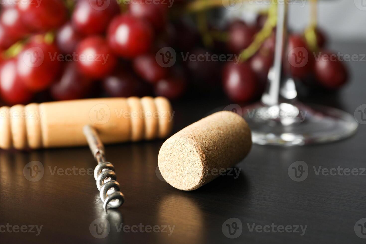 Grapes, corkscrew, cork and wine glass on dark table, close up photo