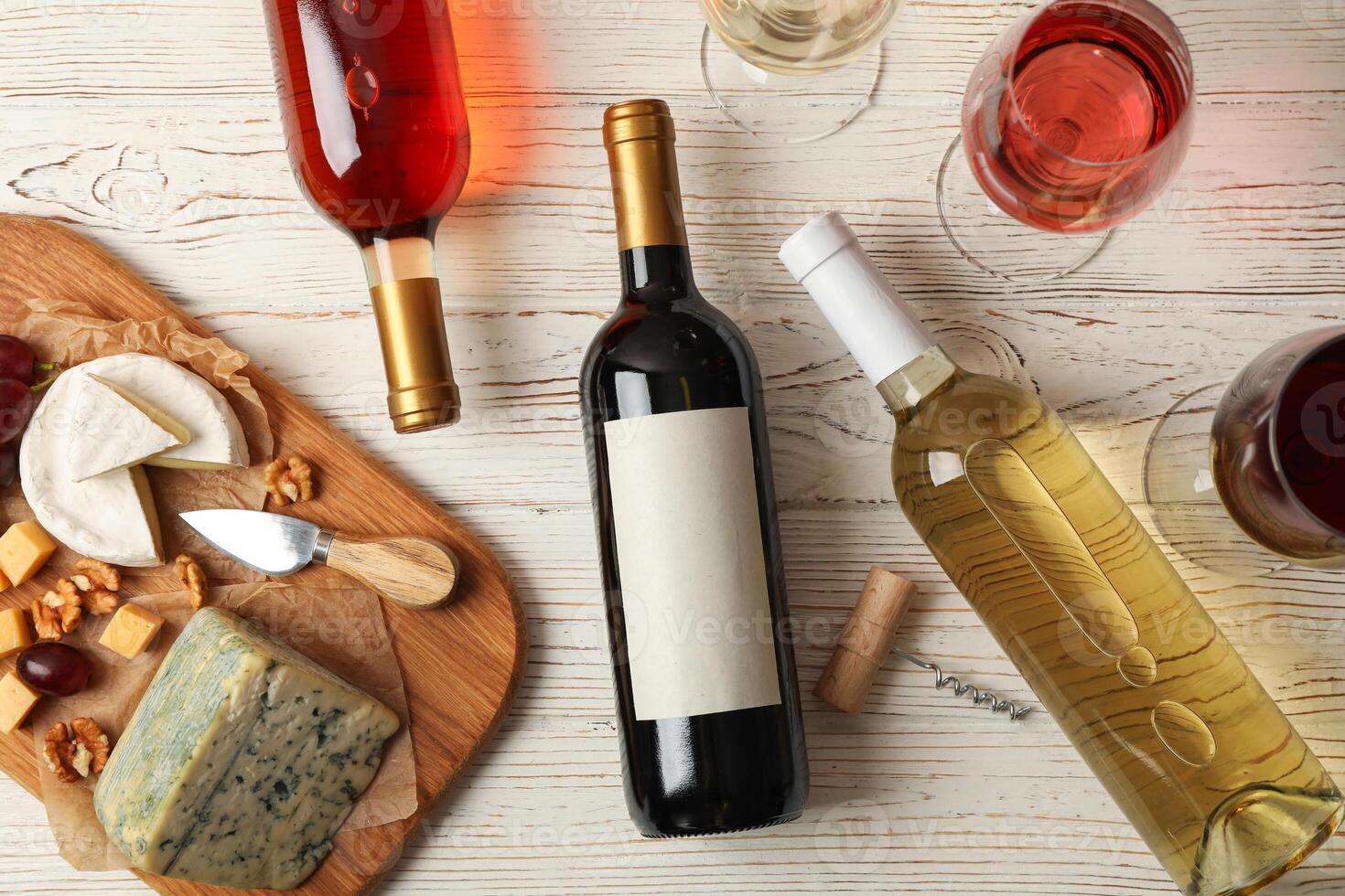 Grape, cheese, bottles and glasses with different wine on white wooden background, top view photo