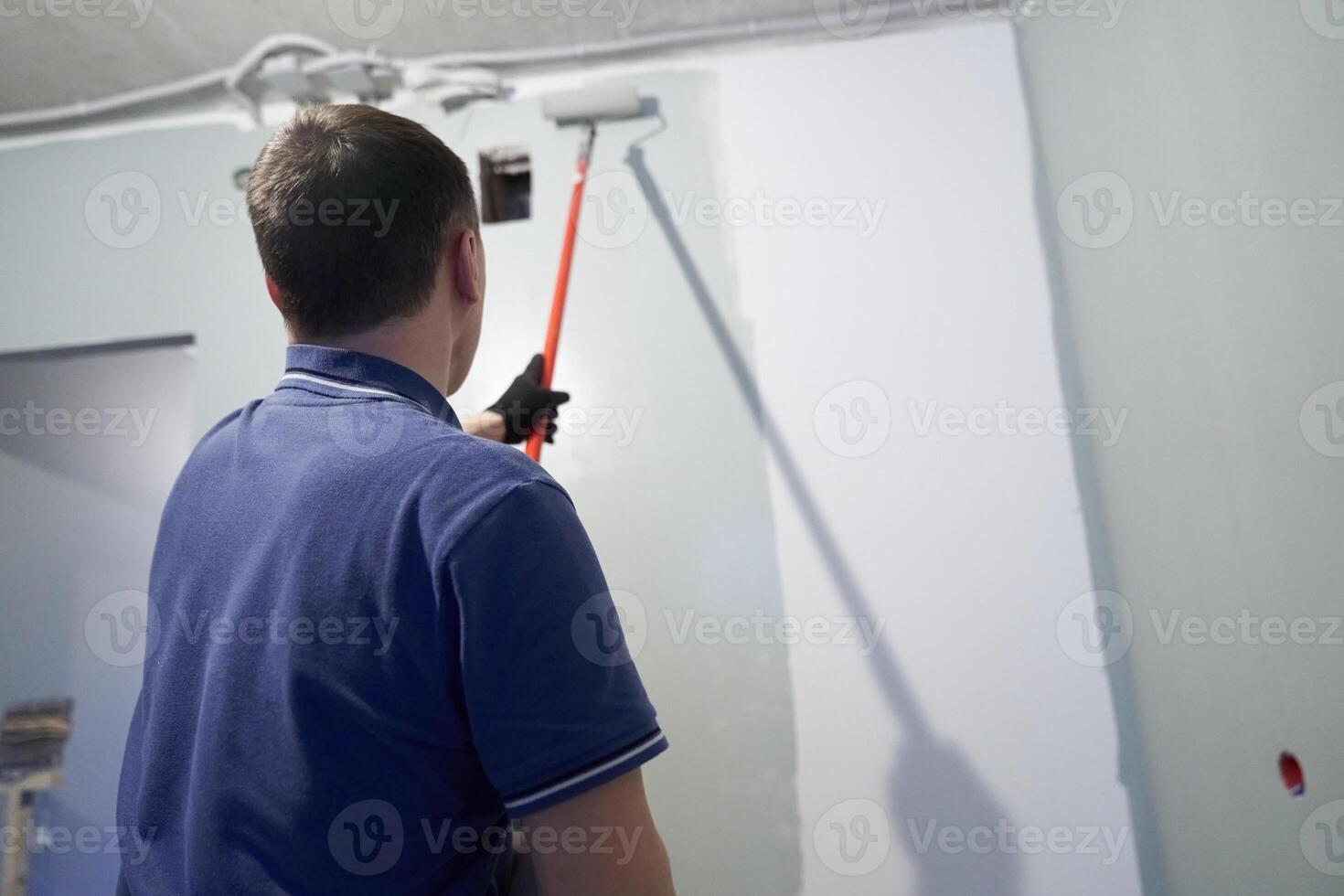 Painting the walls in a vertical line. A man paints concrete walls with a paint roller. Gray paint creates a cozy atmosphere in the room photo