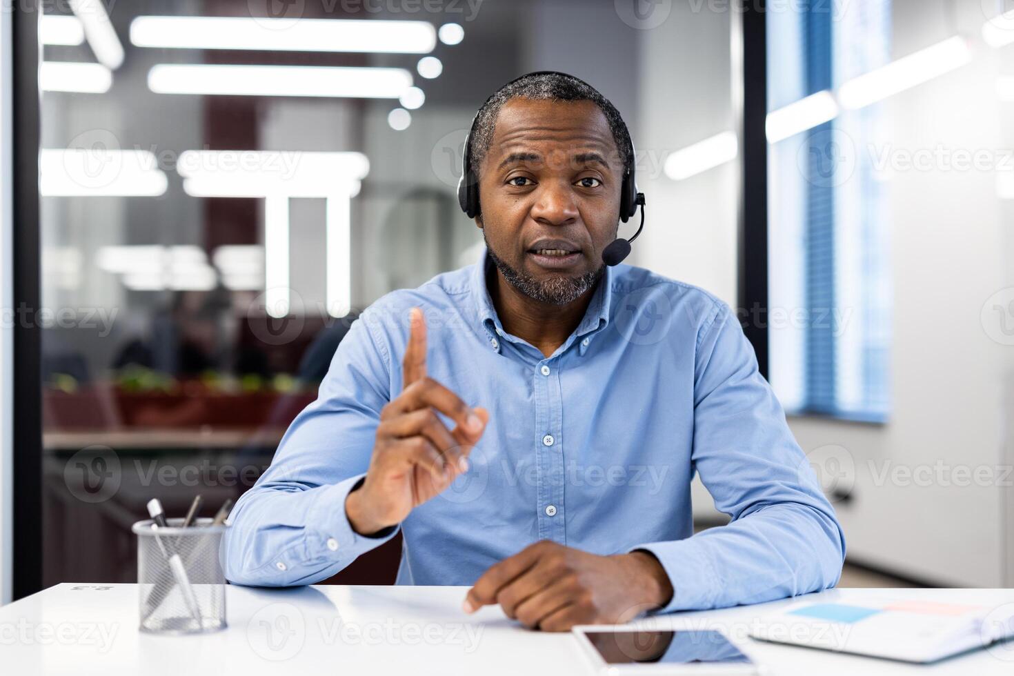 Mature african american businessman wearing headset in modern office during conference. Engaging in discussion with expressive gestures, focused on communication and teamwork. photo