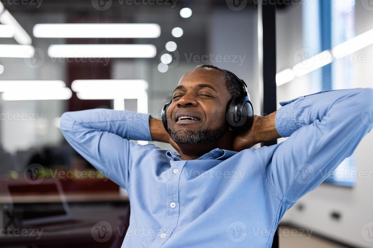 Mature African American businessman relaxing with headphones in office. Enjoying music, feeling stress-free. Calm expression suggests contentment and peace during work break. Perfect for relaxation. photo