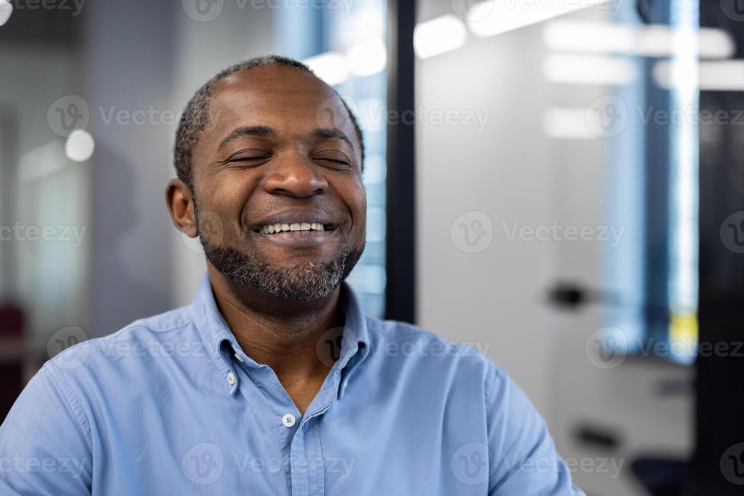 Mature african american businessman in modern office smiling with closed eyes, expressing happiness, relaxation, and success. Professional setting creates calming and positive work environment. photo