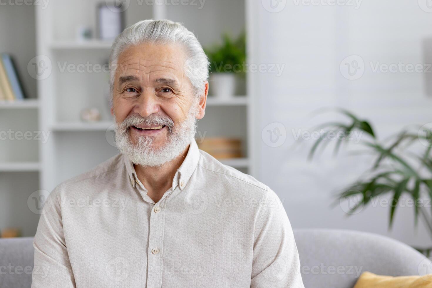 Smiling senior man with white beard sitting in a bright modern living room, exuding happiness and wellness. photo