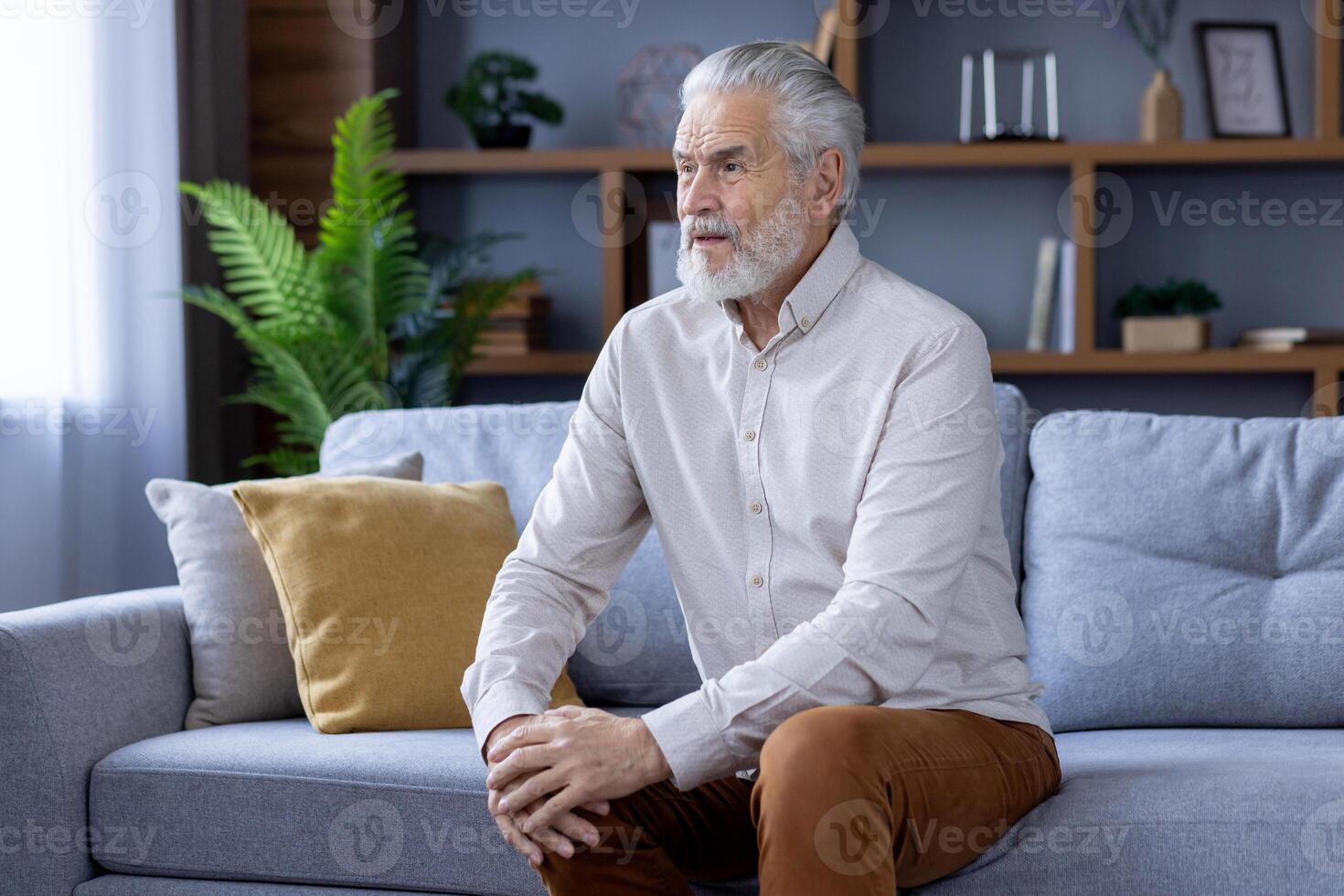 Sick senior gray-haired man suffering from pain and sprained leg, arthritis and varicose veins. Sitting at home on the sofa and holding hands on the knee. photo