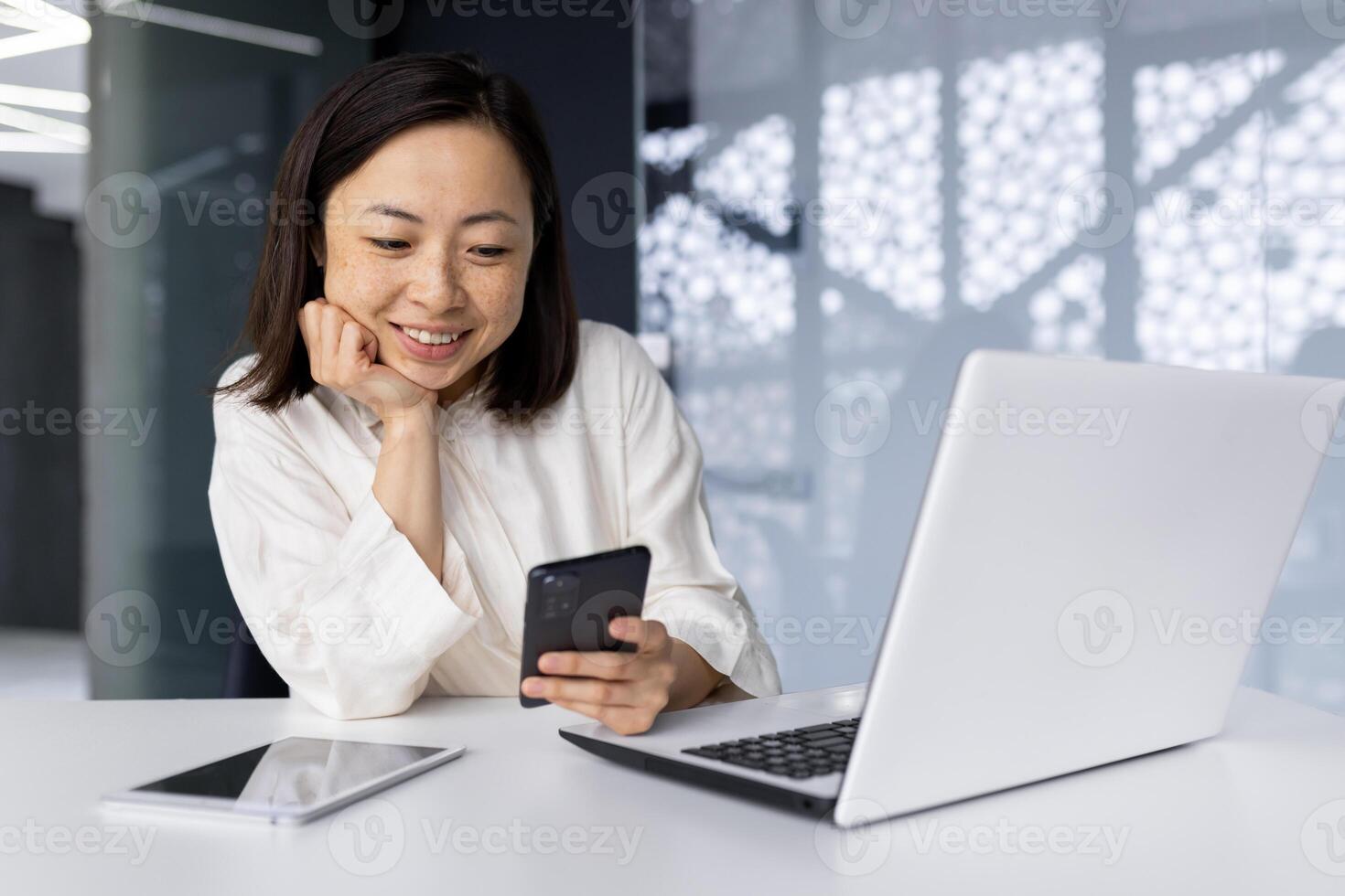 Asian business woman smiling and working at the workplace inside the office, businesswoman reading news using smartphone, boss with laptop using phone and browsing internet pages online. photo