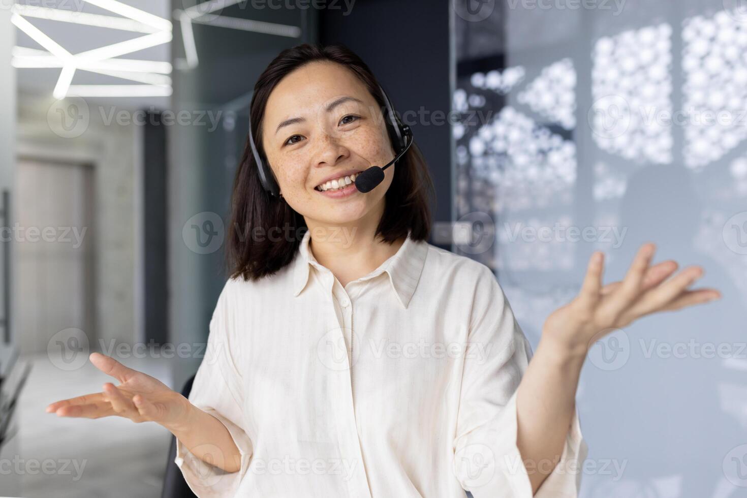 Businesswoman with call headset smiling and looking at camera, Asian woman talking to customers remotely, tech support worker talking, webcam view photo