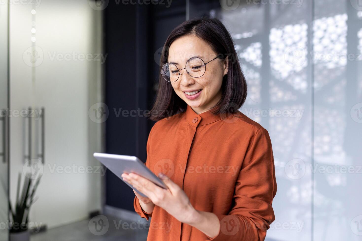 Smiling Asian young female programmer standing in office and working on tablet. photo